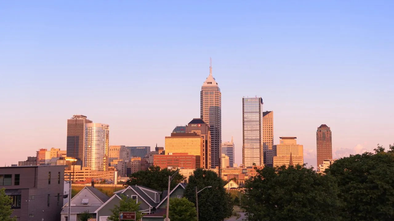 The downtown Indianapolis skyline glowing at sunset, seen over the rooftops of a nearby residential neighborhood