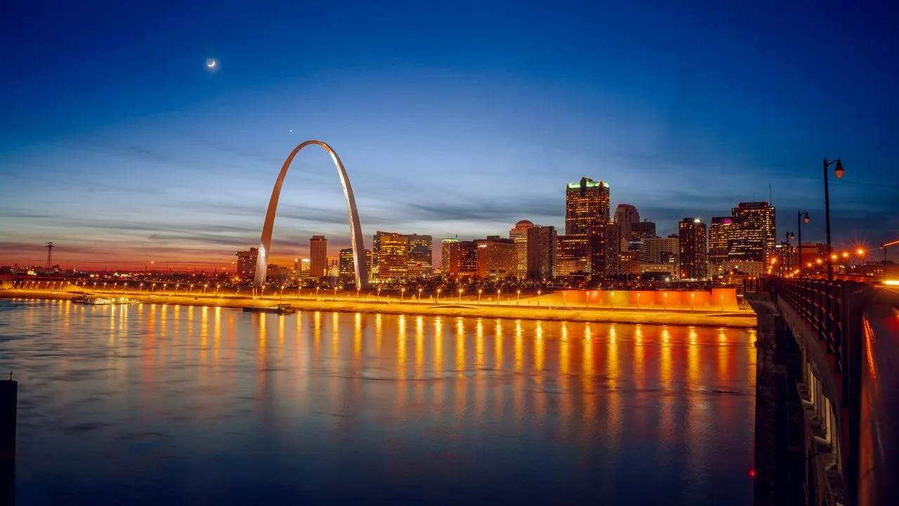 The Gateway Arch and the downtown St. Louis, Missouri skyline at dusk, with city lights reflected in the river