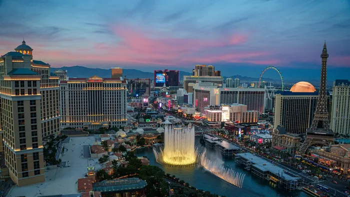 The Las Vegas Strip at twilight seen from above, with the Bellagio fountains in front and the Las Vegas Valley stretching to the mountains