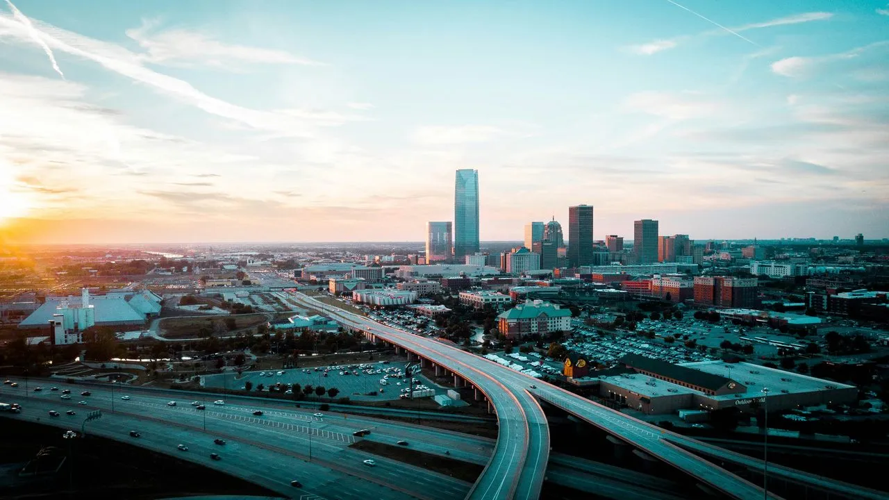 The downtown Oklahoma City skyline at sunset, with Devon Tower rising above the city and highway ramps curving through the foreground