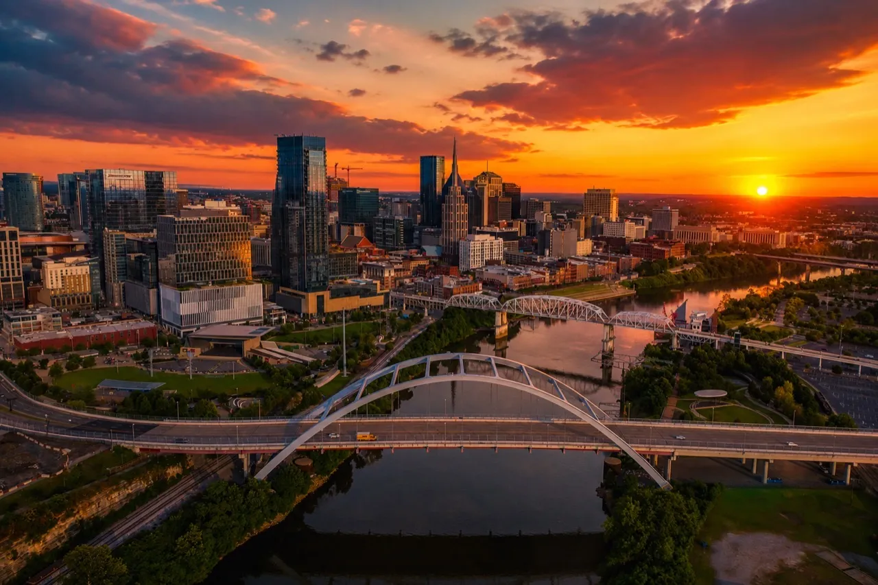 Nashville, Tennessee skyline at sunset over the Cumberland River with an arched pedestrian bridge in the foreground