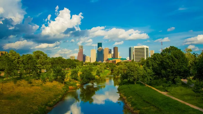 The downtown Houston, Texas skyline rising beyond a tree-lined bayou and green parkland